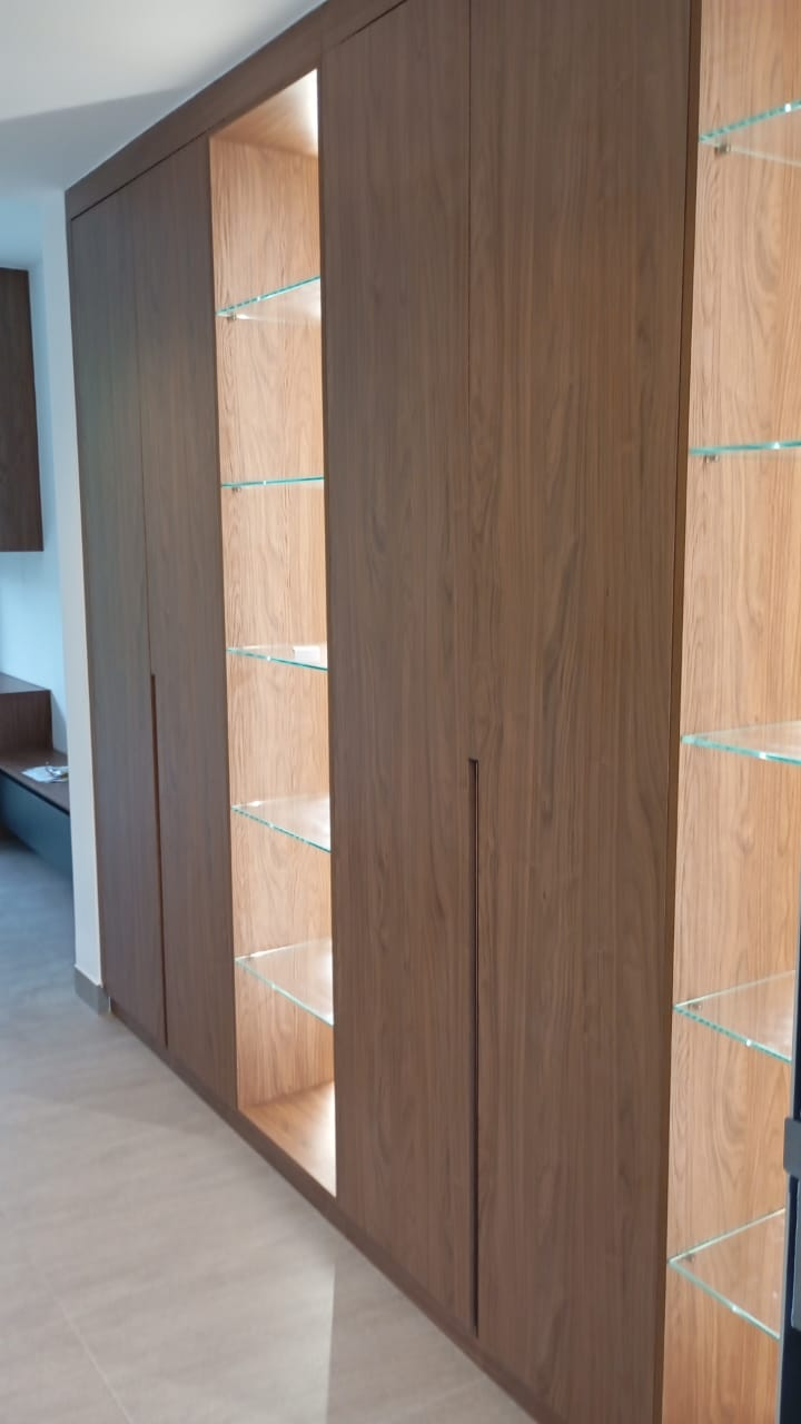 tall walnut wardrobe doors opening to reveal glass display shelves with integrated lighting