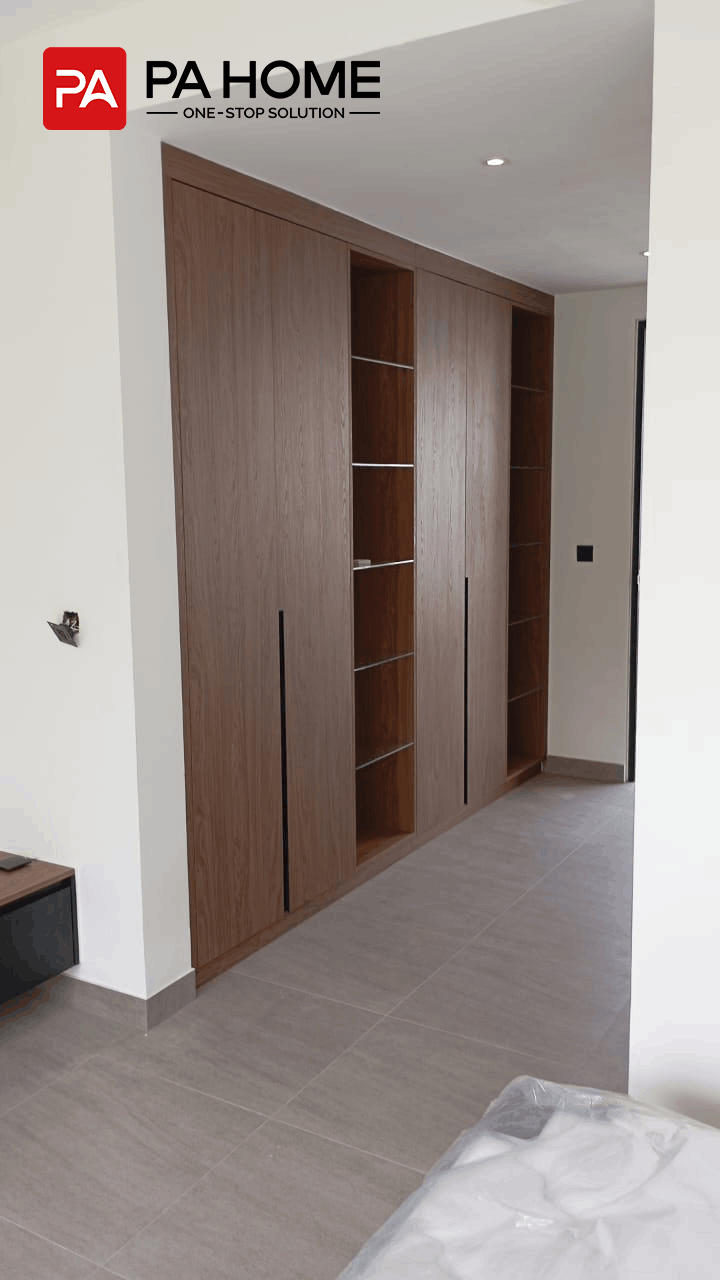 Vila 4 Kamar Tidur di Bali dengan Lemari dan Furnitur Built-In Sesuai Pesanan 1 Lemari pakaian built-in di vila Bali dengan pintu berwarna kayu, rak kaca, dan pencahayaan terintegrasi.