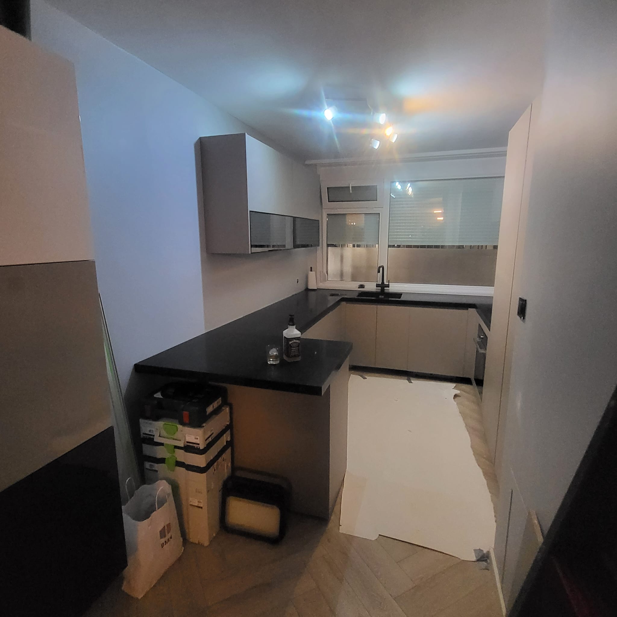 U-shaped modern kitchen cabinet with black countertop and upper wall cabinets under track lighting
