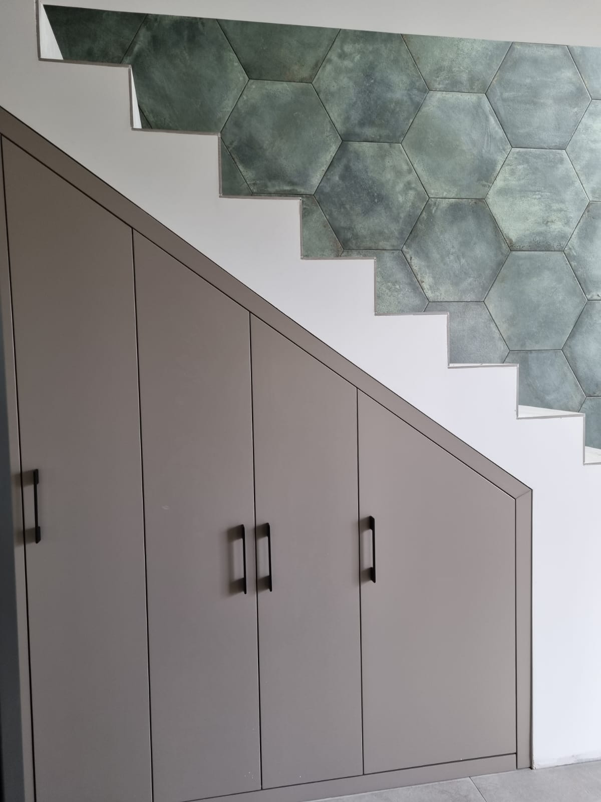 Under-stairs stair cabinet with matte grey doors and black handles in this France stair cabinet case