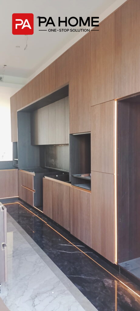 Renovasi Rumah di Indonesia dengan Kabinet Dapur dan Lemari Pakaian Kamar Tidur yang Dibuat Sesuai Pesanan 12 Kabinet dapur kustom motif serat kayu dengan panel bergaris, area kerja berwarna gelap, dan pencahayaan terintegrasi di sebuah rumah di Indonesia.