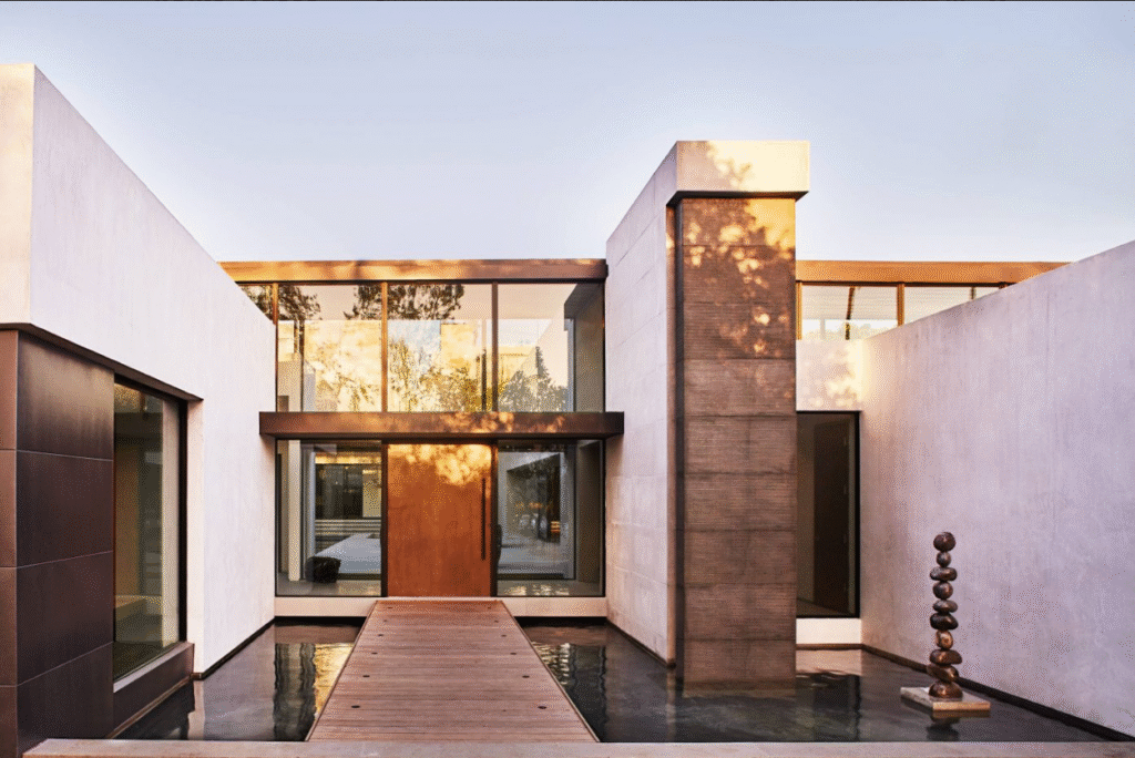 Modern villa facade with floor-to-ceiling aluminum windows and doors along a reflective water-lined entrance pathway