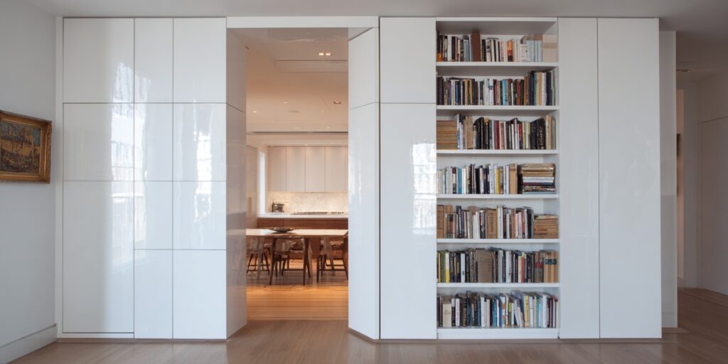 White bookshelf wall with an invisible door integrated into cabinetry leading to another room.
