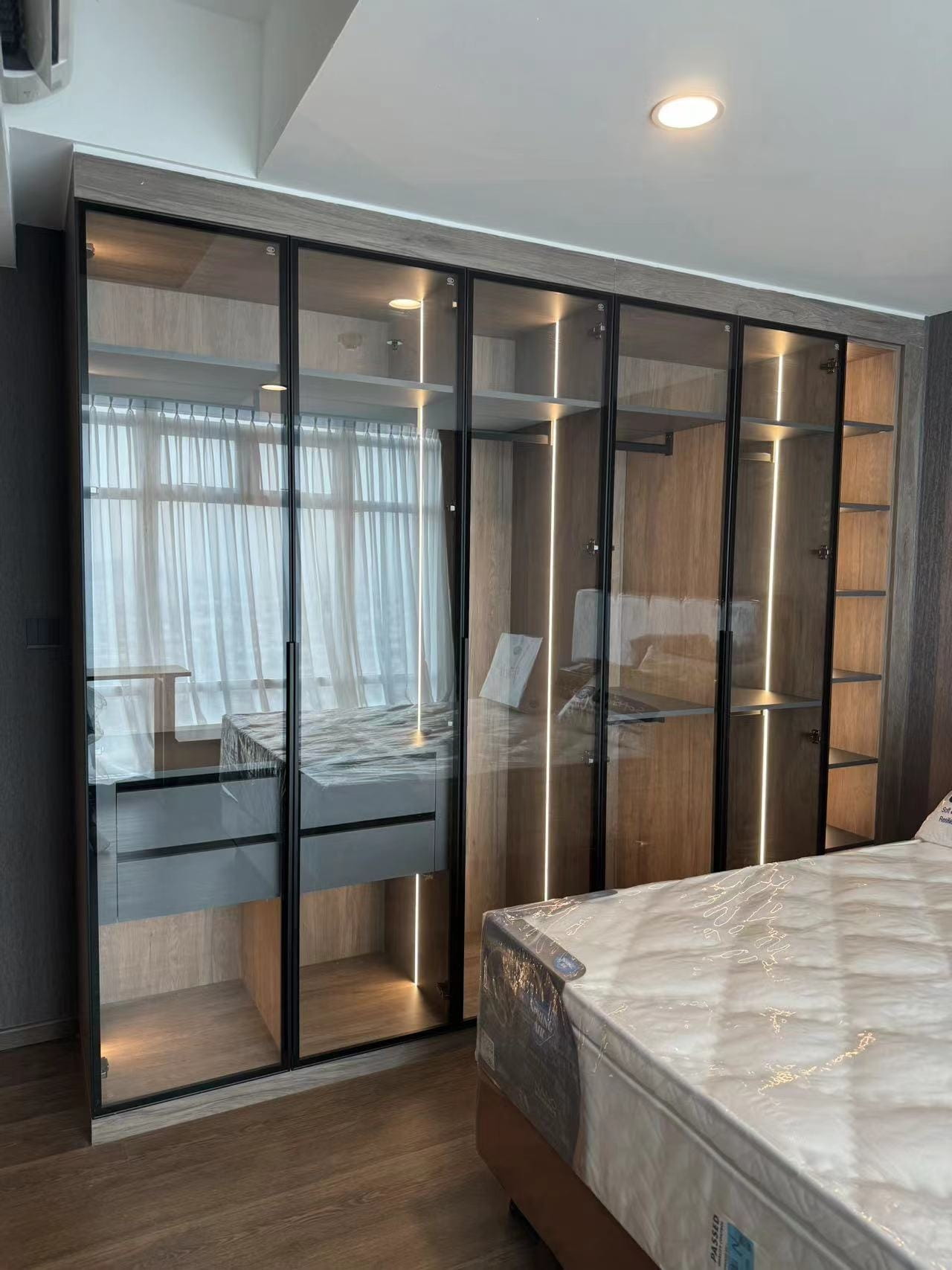Medan Manhattan Apartment Renovation in Indonesia 5 Medan apartment renovation bedroom with black-framed glass wardrobe and built-in lighting.