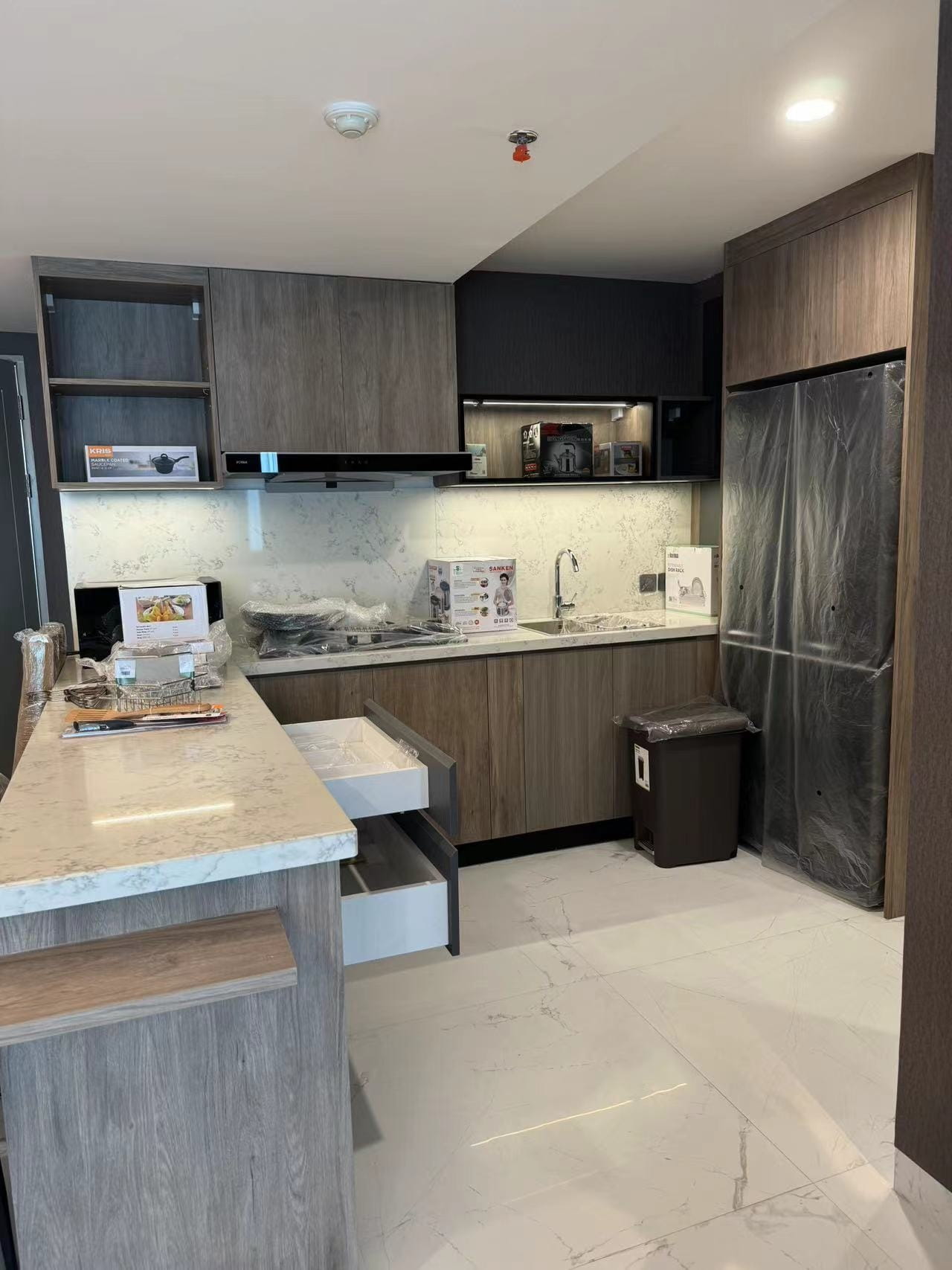 Medan Manhattan Apartment Renovation in Indonesia 8 Custom L-shaped kitchen cabinets with wood grain finish, under-cabinet lighting, and tall refrigerator cabinet.