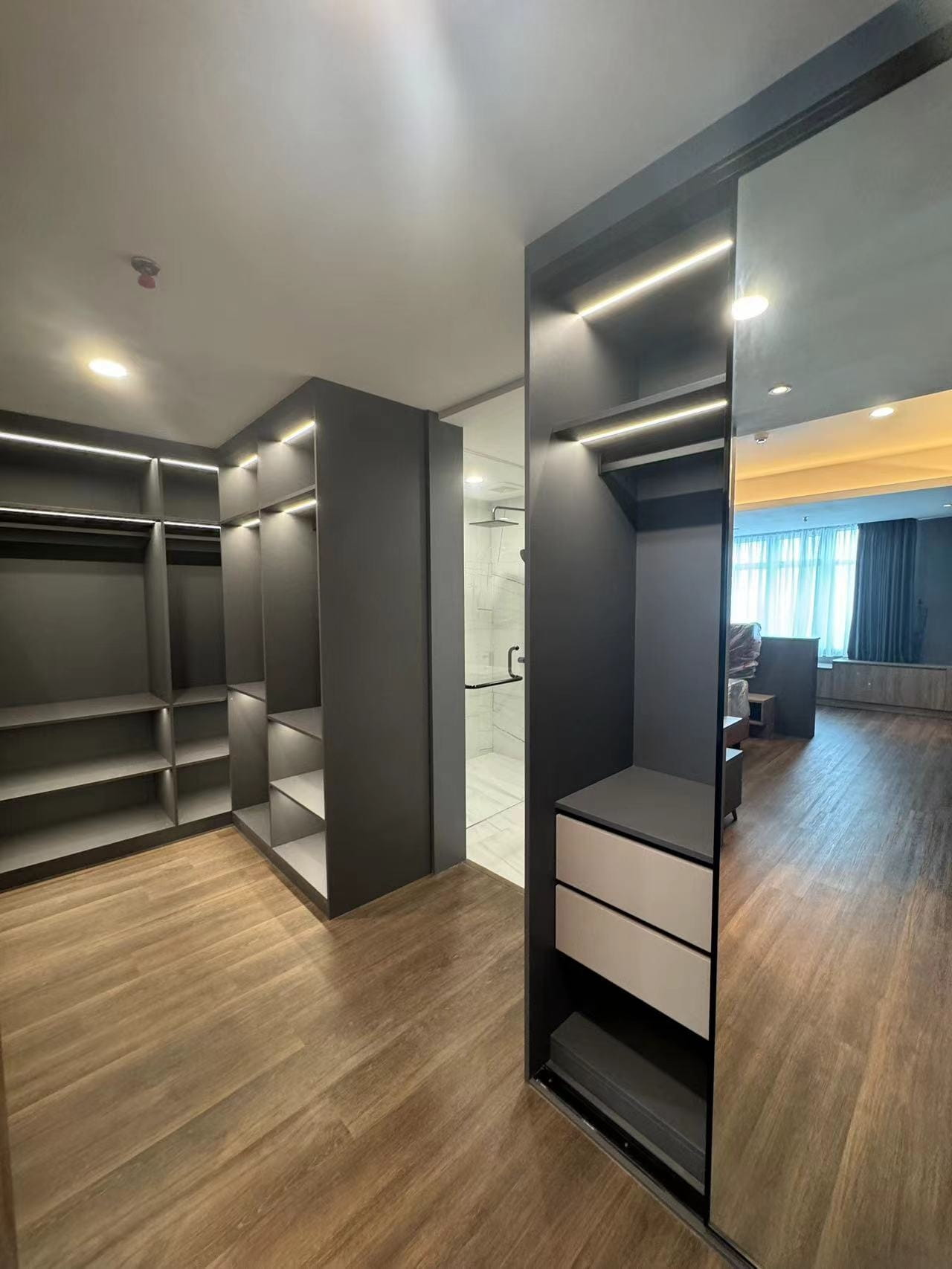 Medan Manhattan Apartment Renovation in Indonesia 11 Medan apartment renovation walk-in closet with LED lighting, open shelves, hanging space, storage drawers., and mirror sliding door.