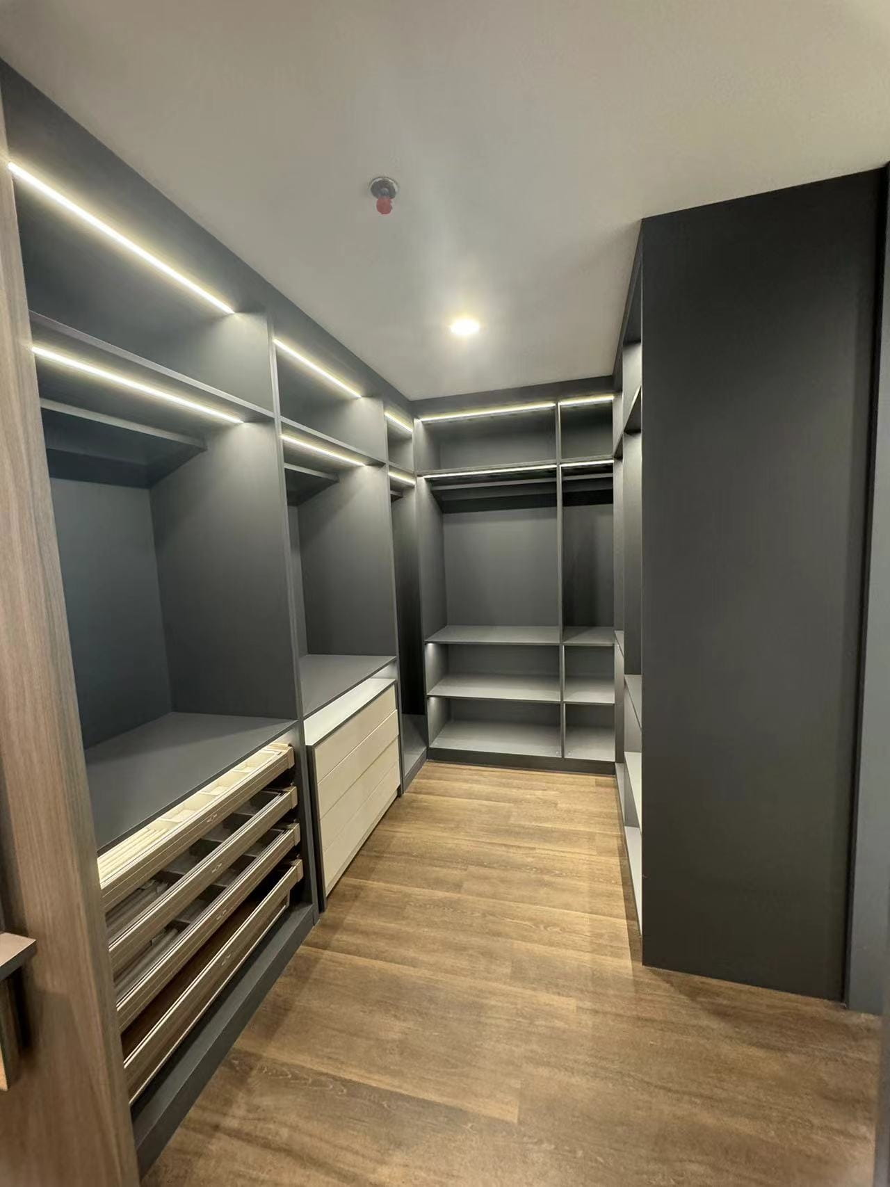 Medan Manhattan Apartment Renovation in Indonesia 12 Open walk-in closet with dark cabinets, hanging rails, shelves, drawers, and integrated lighting.