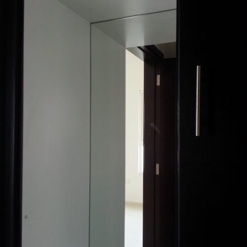 In this Abu Dhabi apartment whole house custom project, the storage cabinet features silver metal handles and a sliding track system, with an integrated mirror.