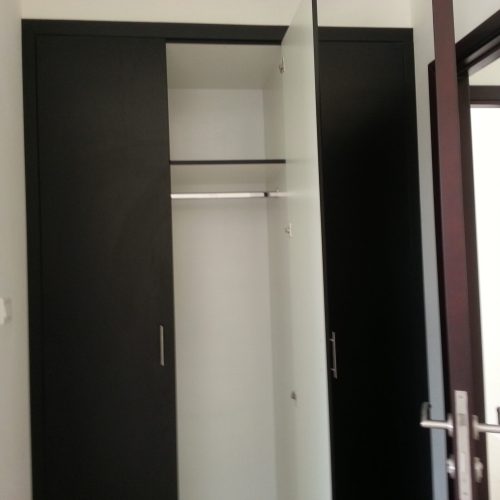 A custom wardrobe with a black exterior and white interior, featuring space for hanging clothes. The adjacent interior door and frame are in a rich burgundy color, adding a touch of elegance to the room.