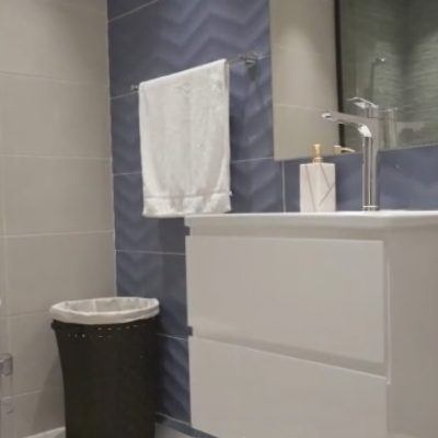 In this Dubai luxury whole house custom project, the bathroom features blue-gray wall tiles, a white vanity, and a mirror, creating a calm and modern aesthetic.