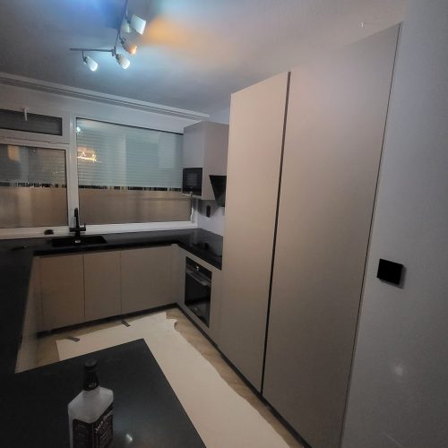 U-shaped modern kitchen cabinet with black countertop and upper wall cabinets under track lighting