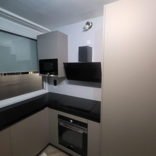 U-shaped modern kitchen cabinet with black countertop and upper wall cabinets under track lighting