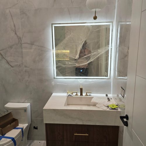 Bathroom with a custom dark wood vanity, marble countertop, and illuminated mirror.