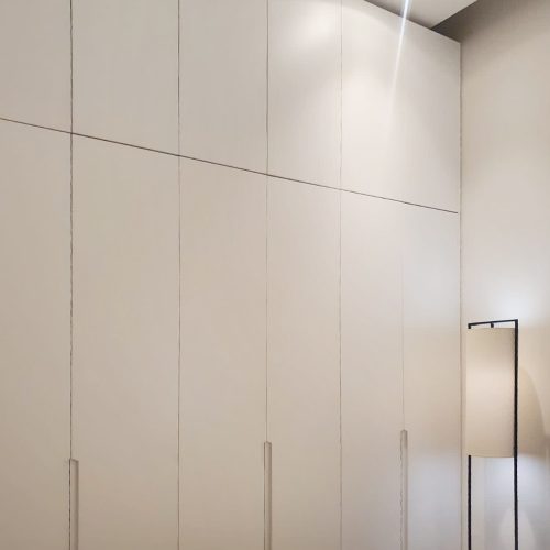 Custom wardrobe with minimalist design and sleek white finish, featuring integrated handles and modern lighting.