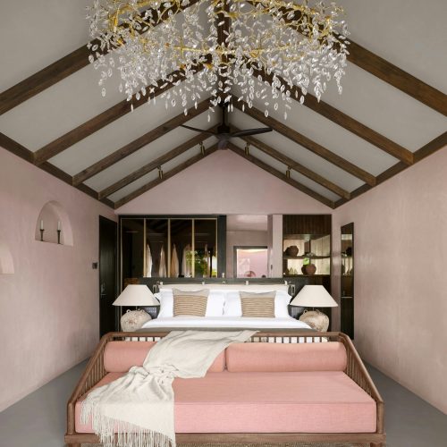 vaulted ceiling bedroom with crystal chandelier and pink sofa bench at foot of king bed