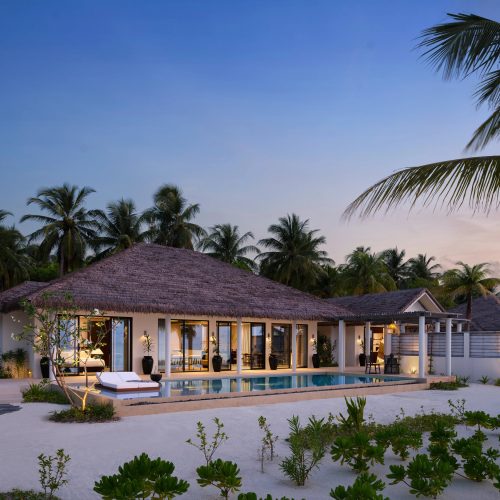tropical villa exterior with beachfront pool and palm trees at sunset