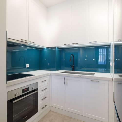 Modern kitchen design with sleek white cabinetry and blue backsplash in the Zemun stan apartment project.